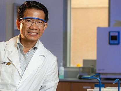 Man is wearing safety goggles and lab coat smiling for a picture