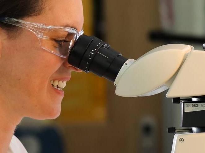 Woman with safety goggles looking through biology microscope