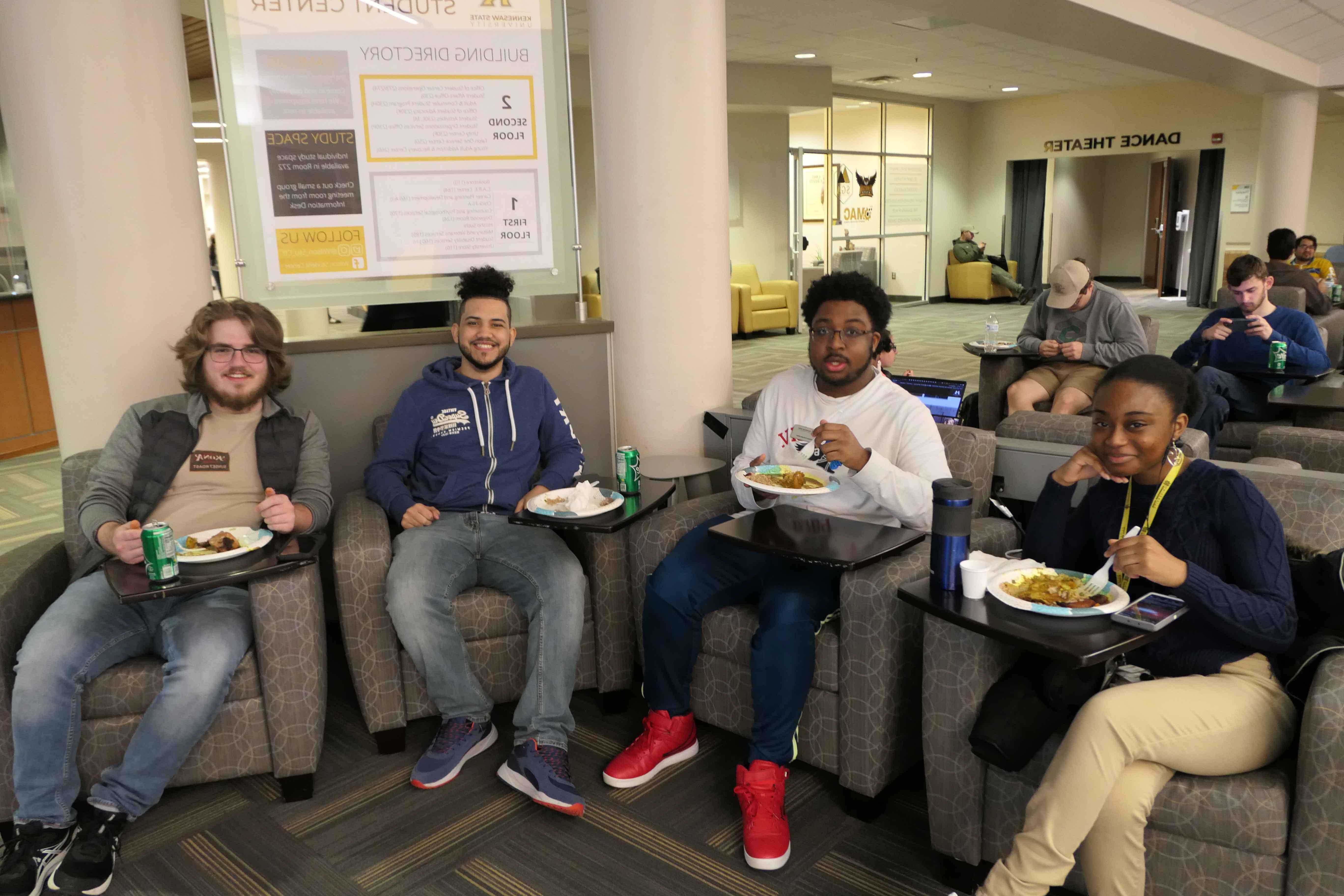  一群ksu学生懒洋洋地坐在椅子上，吃着一盘食物.
